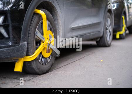 Gelbes Radschloss an einem zufälligem Auto auf der Straße. Verstoß gegen das Parken, gemeinsame Strafe für das Blockieren eines Autos aus dem Verkehr Stockfoto