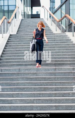 Von unten voller Körper der modernen jungen Frau in stilvollem Outfit mit Tasche zu Fuß Treppe in der Stadt im Sommer Tag Stockfoto