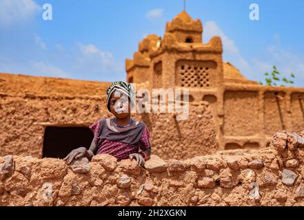 Ein Mädchen, das von einer Mauer im Dorf Yamma in Niger aus zusieht Stockfoto