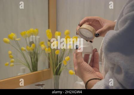 Junge männliche Hand im Bademantel hält Gesichtscreme nach der Rasur anzuwenden. Beauty Home Spa-Konzept. Stockfoto