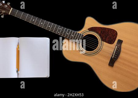 Klassische Akustikgitarre und ein offenes Notizbuch auf schwarzem Hintergrund. Stockfoto