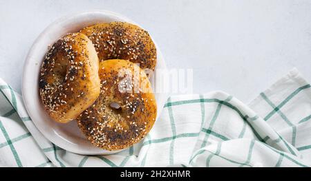 Bagels in einer alten Keramikschale mit einer textilen Serviette auf einem hellen Stein- oder Betongrund. Selektiver Fokus. Draufsicht. Speicherplatz kopieren. Stockfoto