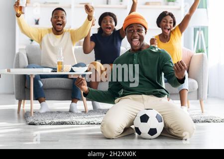 Glückliche afroamerikanische Fußballfans, die ein Spiel im Fernsehen anschauen Stockfoto