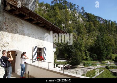 Blick mit Touristen von Predjama Castle, Grad Predjama gebaut in einer Höhlenmündung in der Nähe von Postojna. Renaissance Schloss, Natur, Klippe, Bäume, Slowenien, Stockfoto