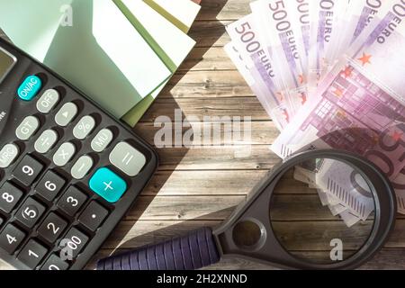 Euro-Banknoten, Taschenrechner und Lupe auf Holztisch Stockfoto