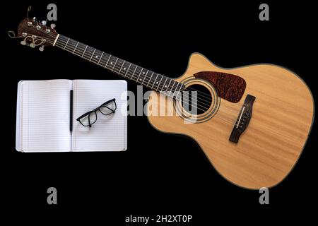 Klassische Akustikgitarre und ein offenes Notizbuch auf schwarzem Hintergrund. Stockfoto