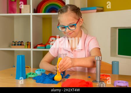 Ein Mädchen mit Down-Syndrom spielt mit buntem kinetischem Sand Stockfoto