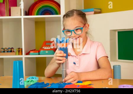 Ein Mädchen mit Down-Syndrom spielt mit buntem kinetischem Sand Stockfoto