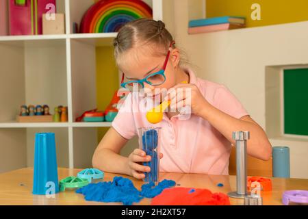 Ein Mädchen mit Down-Syndrom spielt mit buntem kinetischem Sand Stockfoto