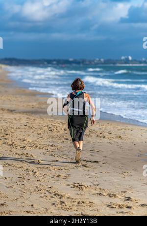 Ältere Frau läuft am Strand, Dame mittleren Alters läuft am Meer, Frau läuft am Sandstrand entlang, läuft am Meer, läuft am Sandstrand. Stockfoto