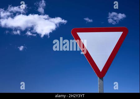 Detail eines Give-Way-Verkehrszeichens über einem blauen und bewölkten Himmel Stockfoto