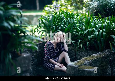 Eine Frau auf einer Steinbank im Grünen in einem alten Park, Porto, Portugal. Stockfoto