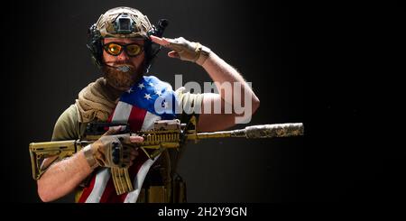 Foto eines amerikanischen Soldaten hält eine Flagge auf seiner Schulter und grüßt. Konzept des Tages der Erinnerung an Veteranen. Stockfoto