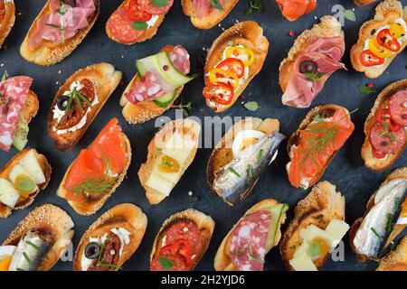 Köstliche gemischte spanische Tapas mit typischen Spezialitäten auf gebratenem Baguette mit Sesam auf dunklem Hintergrund Stockfoto