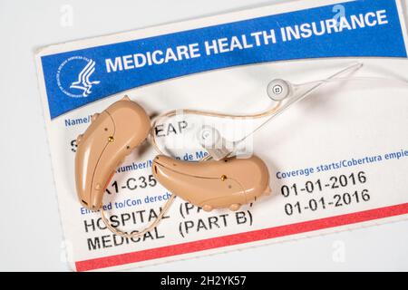Makro-Nahaufnahme eines zusammenpassenden Paares von winzigen modernen Hörgeräten auf Medicare-Karten-Hintergrund, da die Abdeckung verbessert wird Stockfoto
