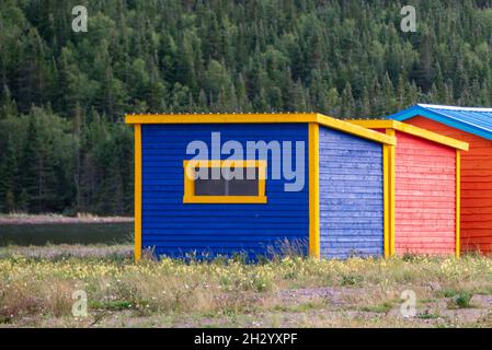 Mehrere bunte Schuppen oder Lagergebäude auf einem Feld mit Bäumen. Eine ist blau und die anderen rot. Alle Lagereinheiten haben eine leuchtend gelbe Zierleiste. Stockfoto