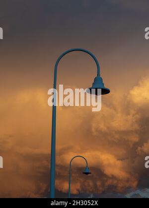 Geschwungene Armlampe steht vor einer dramatischen Sturmwolke, die den Himmel in rosa-oranger Farbe widerspiegelt, der sich vom Sonnenuntergang, der Anlegestelle, Coffs Harbour Australia, widerspiegelt Stockfoto