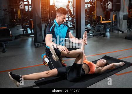 Junge Frau trainiert tote Käfer mit Personal Trainer im Fitnessstudio Stockfoto