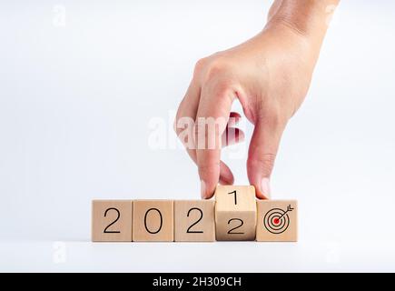 Das Kalenderjahr 2021 wurde mit dem Ziel und dem erfolgreichen Konzept auf 2022 geändert. Handdrehende Holzwürfelblöcke für den Übergang von 2021 auf 2022 mit Stockfoto