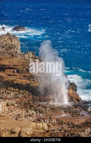 Ein Paar (MR) bekommt einen näheren Blick auf das Nakalele Blowhole, das Wasser sprießt, an der Nordküste von Maui, Hawaii. Stockfoto