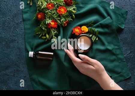 Weibliche Hand mit Kosmetikprodukten und Ringelblumen auf dunklem Hintergrund Stockfoto