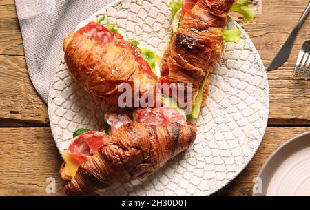 Teller mit leckeren Croissant-Sandwiches auf Holzhintergrund Stockfoto