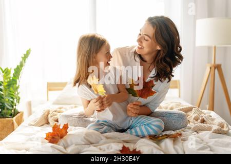 Ein nettes Mädchen und ihre Mutter genießen sonnigen Morgen. Gute Zeit zu Hause. Kind wacht aus dem Schlaf auf. Familie spielt auf dem Bett im Schlafzimmer. Stockfoto