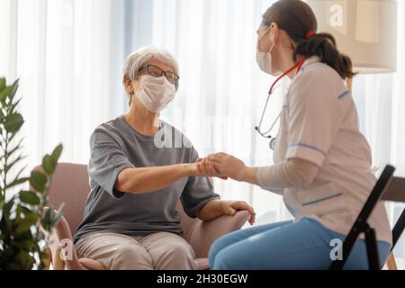 Arzt und ältere Frau mit Gesichtsmasken während des Coronavirus- und Grippeausbruchs. Virenschutz. COVID-2019. Masken übernehmen. Stockfoto