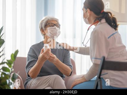 Arzt und ältere Frau mit Gesichtsmasken während des Coronavirus- und Grippeausbruchs. Virenschutz. COVID-2019. Masken übernehmen. Stockfoto