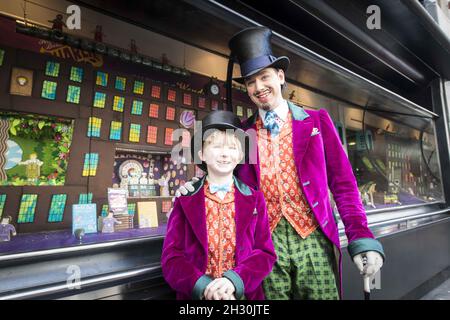 Willy Wonka (Ross Dawes) und Charlie (Troy Tipple) stehen für eine Fotocolade vor einer Schokoladenfabrik in Keksform, die vom West End Musical und Biscuiteers, unterstützt von Tate und Lyle, zum 50. Jahrestag von Roald Dahls Charlie und der Schokoladenfabrik nachgebildet wurde, Im Schaufenster der Waterstones, Piccadilly, London. Stockfoto