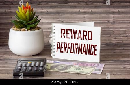 Geschäftskonzept. Notizblock mit dem Text BELOHNEN LEISTUNGSBLATT aus weißem Papier für Notizen, Rechner, Kaktus und Banknoten von Dollar und Euro auf einem Stockfoto