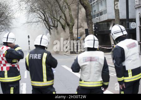 Feuerwehrmann beobachtet, wie Rauch aus einem unterirdischen Kabelbrand auf Kingsway, bei Holborn - London, aufsteigt Stockfoto