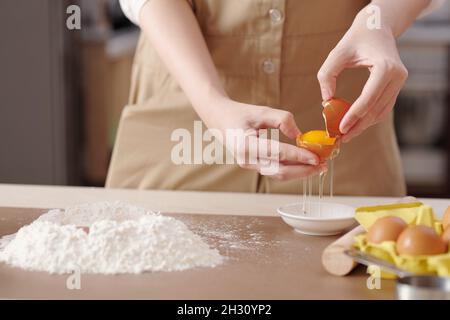 Hände einer jungen Frau, die Eigelb vom Eiweiß trennt, wenn der Teig gemacht wird Stockfoto