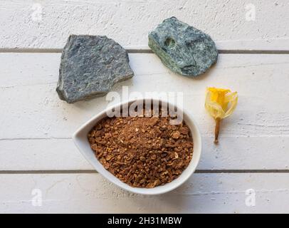 Tasse Haferflocken auf einer weißen Holzplatte mit Steinen und Blumendekoration Stockfoto