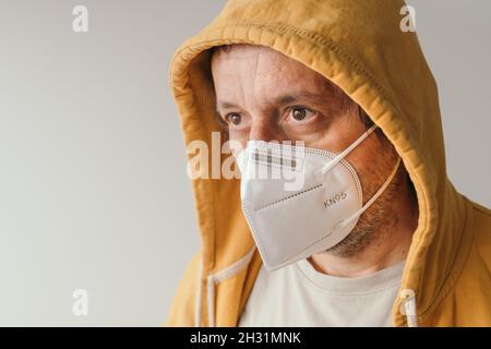 Lässiger Mann mit gelber Kapuzenjacke, der eine schützende Atemschutzmaske KN95 während der Covid-19-Pandemien trägt, selektiver Fokus Stockfoto