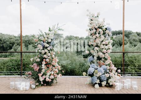 Ein wunderschöner Hochzeitbogen, geschmückt mit Blumen und viel Grün, in der Nähe eines Sees oder Flusses im Freien. Dekorationen für eine Hochzeit im Freien Stockfoto