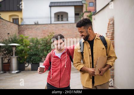 Junger Mann mit Down-Syndrom und sein Mentor-Freund gehen und reden im Freien Stockfoto