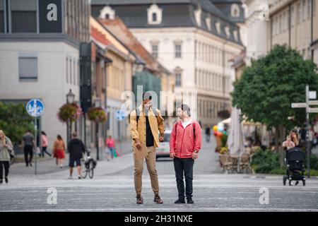 Junger Mann mit Down-Syndrom und sein Mentor-Freund gehen und reden im Freien Stockfoto