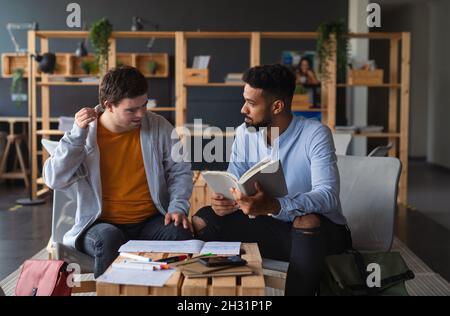 Junger glücklicher Mann mit Down-Syndrom und sein Tutor, der in der Schule drinnen studiert. Stockfoto