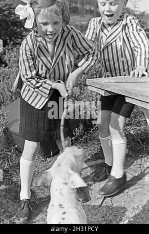 Zwei Kinder in gestreiften Jacketts beim Spielen mit einem Hund, Deutschland 1930er Jahre. Zwei Kinder in gestreiften Jacken spielen mit einem Hund, Deutschland 1930er Jahre. Stockfoto