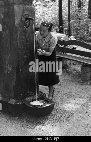 Eine junge Frau probt das Trinkwasser des Eberbrunnens auf einem Wanderpfad bei Baden-Baden im Nordschwarzwald, Deutschland 1930er Jahre. Eine junge Frau verkostet das Trinkwasser des Eberbrunnens auf einem Wanderweg in der Nähe von Baden-Baden im Nordschwarzwald, Deutschland 1930er Jahre. Stockfoto