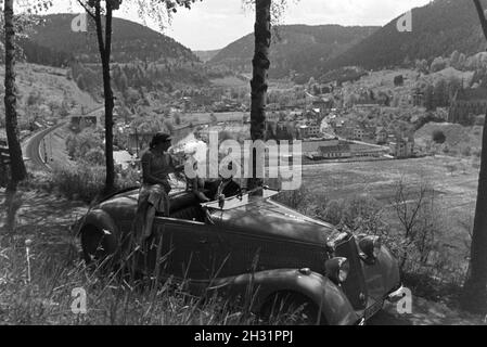 Ein junges Paar und ihr Hund bei einer Spazierfahrt mit dem Mercedes Cabrio in Hirsau im Nordschwarzwald, Deutschland 1930er Jahre. Ein junges Paar und ihr Hund fahren durch Hirsau im Nordschwarzwald in einem Mercedes Cabrio, Deutschland 1930. Stockfoto