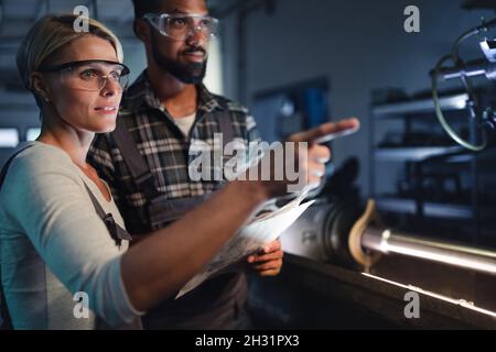 Portrait von jungen biracial Industriekollegen, die sich in einer Metallwerkstatt unterhalten. Stockfoto