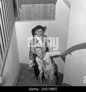 Zwei Jungen toben an Fasching im Cowboykostüm durch das Treppenhaus, Deutschland 1959. Zwei als Cowboy gekleidete Jungen schwärmen an Fasching, Deutschland 1959, durch das Haus. Stockfoto