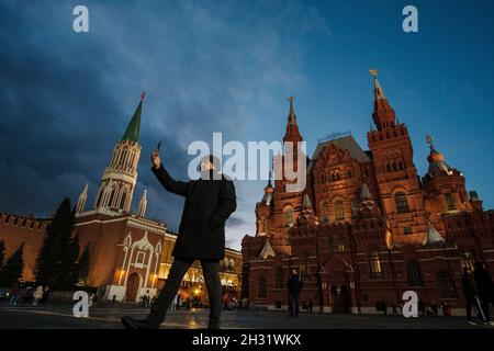 MOSKAU, RUSSLAND - 24 2021. OKTOBER: Mann mit Smartphone zwischen dem Historischen Museum und dem Nikolskaya-Turm Stockfoto