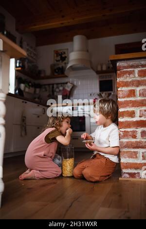 Zwei kleine Kinder drinnen zu Hause, essen Cornflakes auf dem Boden. Stockfoto