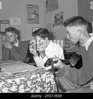 Drei Jungen mit Mundharmonika und Gitarre intonieren ihre Lieblingslieder, Deutschland 1956. Drei Jungs mit Mundharmonika und gutar spielen ihre Lieblingslieder, Deutschland 1956. Stockfoto