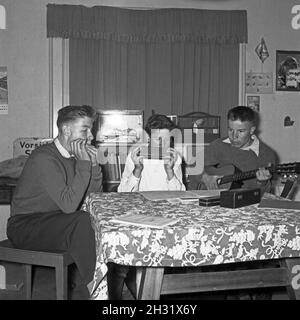 Drei Jungen mit Mundharmonika und Gitarre intonieren ihre Lieblingslieder, Deutschland 1956. Drei Jungs mit Mundharmonika und gutar spielen ihre Lieblingslieder, Deutschland 1956. Stockfoto