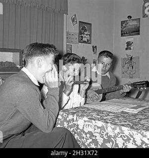 Drei Jungen mit Mundharmonika und Gitarre intonieren ihre Lieblingslieder, Deutschland 1956. Drei Jungs mit Mundharmonika und gutar spielen ihre Lieblingslieder, Deutschland 1956. Stockfoto