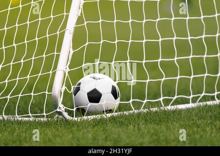 Fußball Ball in einem Tor. Fußball liegt im Gras. Fußballausrüstung. Weißes Fußballtor und Netz Stockfoto
